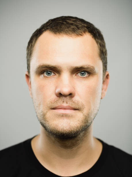 Close up portrait of caucasian young adult man with blank expression against gray background. Vertical shot of real russian man staring in studio with brown hair and green eyes. Photography from a DSLR camera. Sharp focus on eyes.
